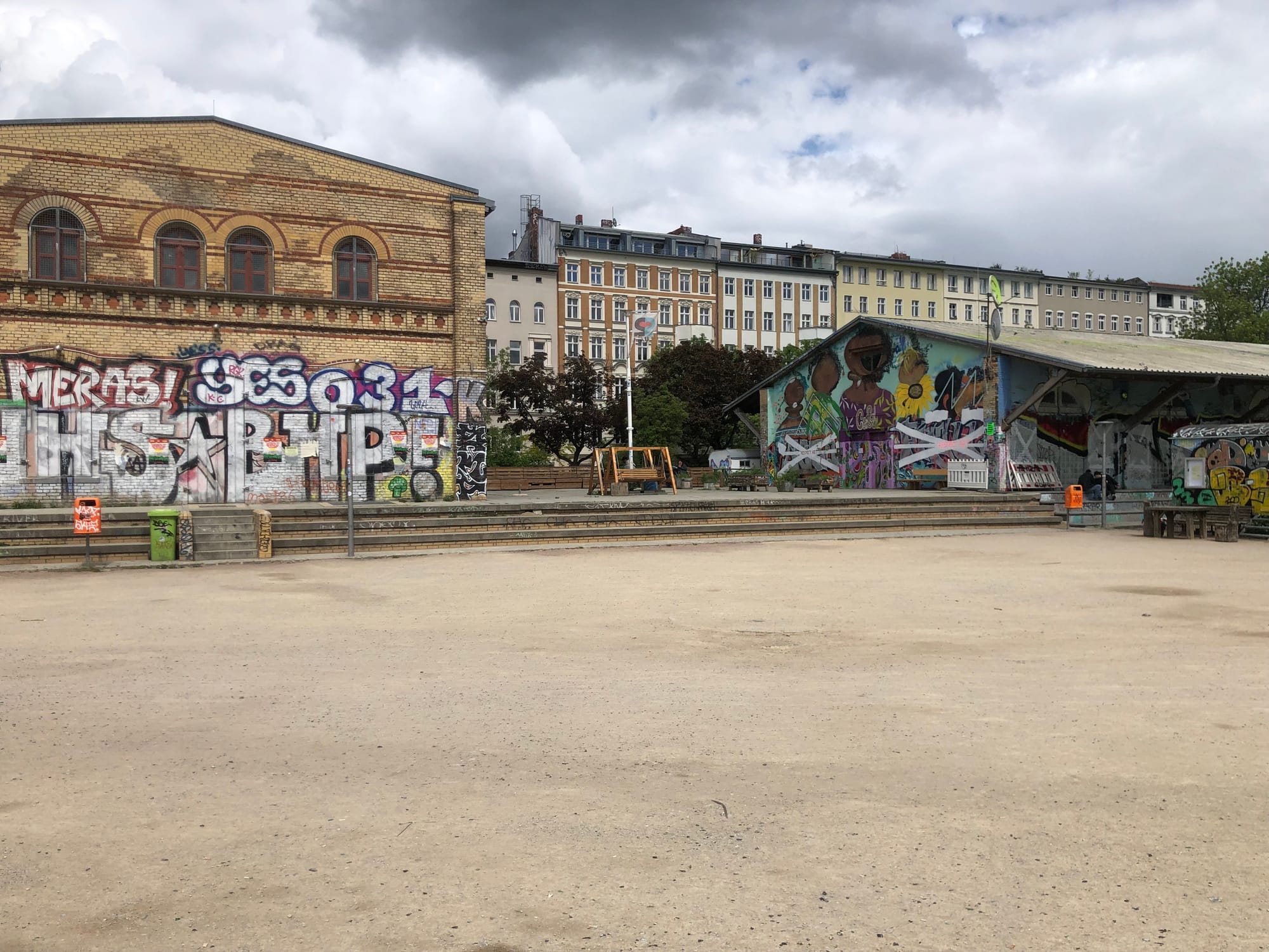 There are two buildings, both of which are boarded up and covered in graffiti. In the background, you can see some apartment buildings. There's a grey sky.